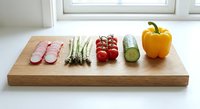 Fresh vegetables arranged on wooden cutting board including sliced radish, asparagus spears, cherry tomatoes, cucumber and yellow bell pepper for cooking.