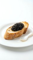 Toasted bread slice topped with black caviar served on white plate with pearl spoon, luxury appetizer for fine dining and gourmet food concepts.