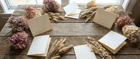 Blank notecards and envelopes arranged with dried flowers and wheat stalks on rustic wooden surface for stationery design mockup.