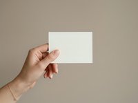 Hand holding blank white card against neutral beige background, suitable for business branding, marketing mockups, and corporate identity design projects.
