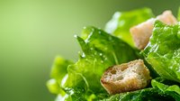 Fresh green lettuce salad with crunchy croutons close-up on blurred background. Crisp leaves with droplets of water and golden bread cubes.