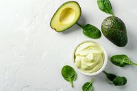 Fresh avocado cream sauce with spinach leaves and halved ripe avocado on light textured background, top view. Healthy vegan dip for appetizers.
