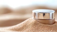 Luxury cosmetic cream jar partially buried in shimmering golden sand with soft focus background, representing beauty, skincare and spa treatments.