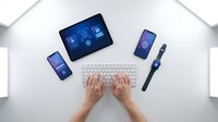 Hands typing on wireless keyboard with tablet smartphone and smartwatch displaying digital interfaces on clean white desk workspace for productivity.