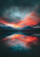 Dramatic sunset sky with vibrant orange and teal clouds reflecting in still mountain lake waters, creating mirror-like symmetry against silhouetted mountain peaks.
