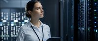 Female IT professional monitoring server infrastructure in data center facility with network equipment and monitoring systems.