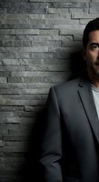 Middle-aged man with dark hair and beard, wearing charcoal blazer over white shirt, posed against textured gray stone wall. Corporate portrait for business, professional headshot, and executive branding use.