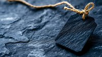 Black slate price tag with natural twine string on dark stone background, creating rustic minimalist composition for retail and craft product labeling.
