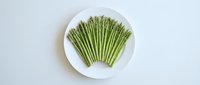 Fresh green asparagus spears arranged on white plate against clean background for healthy cooking and nutrition concepts.