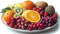 Fresh tropical and berry fruits arranged on white ceramic plate including oranges, kiwi, pineapple, bananas, raspberries and red grapes for healthy eating concept.