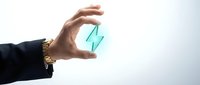 Young adult male hand with medium skin tone wearing black sleeve and gold bracelet holding transparent turquoise glass or acrylic geometric shape against white background for business concepts.