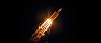 Powerful rocket launch with bright orange flames and smoke trail against dark night sky, space exploration mission takeoff with dramatic lighting effects.