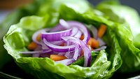 Fresh green lettuce leaf filled with sliced purple onion rings and carrot pieces on dark plate, macro food photography with selective focus.