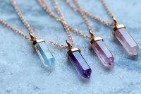 Rose gold chain necklaces with crystal quartz pendants in purple, pink and clear colors on marble surface for jewelry design and fashion accessories.