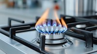 Gas stove burner with blue and orange flames on modern kitchen cooktop, close-up view showing clean stainless steel surface and precise flame control.