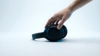 Caucasian male hand with ring reaching for black over-ear wireless headphones on white background, music and technology concept.