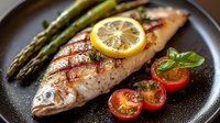 Grilled fish fillet with lemon slice, cherry tomatoes, and asparagus on dark plate, showcasing healthy Mediterranean cuisine.