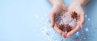 Female hands holding pink bath salt crystals with star anise spices for aromatherapy spa treatment on light blue background with scattered salt.