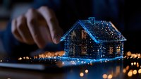 Glowing blue hologram house projection over digital tablet with bokeh lights in dark room, futuristic smart home technology concept.