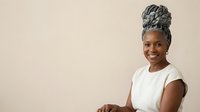 Mature African American woman with gray hair styled in an updo, wearing a white t-shirt, smiling at camera against neutral background. Portrait for diversity, age representation, and professional use.