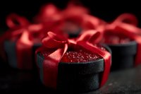 Elegant black velvet gift box with luxurious red satin ribbon bow and sparkling contents on dark background, creating romantic and mysterious atmosphere.