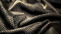 Close up of metallic silver carbon fiber textile with wave pattern and light reflection creating dynamic surface texture and modern technological look.