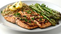 Grilled salmon fillet with quinoa, roasted asparagus and lemon on white plate. Fresh herbs garnish seafood dinner featuring protein-rich ingredients and seasonal vegetables.