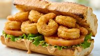 Crispy golden onion rings piled high on fresh sandwich with lettuce and sauce on toasted bun. Fast food comfort meal for restaurant menus and advertising.