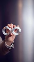 Hand holding silver infinity symbol against blurred background, representing endless possibilities, continuous growth, and limitless potential for business and personal development concepts.