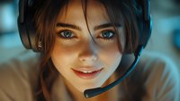 Young woman with bright blue eyes wearing gaming headset smiles warmly in atmospheric blue lighting, close-up portrait showing genuine happiness and engagement.