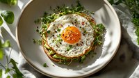 Fried egg with crispy toast, microgreens, and herbs served on white plate for breakfast, brunch, or culinary content.