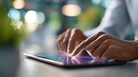 Close up view of hands typing on digital tablet touchscreen with soft bokeh background lights, modern workplace technology and mobile computing.