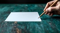 Hand holding wooden pencil over blank white paper on dark turquoise wooden table background, ready for creative writing, drawing or sketching. Artistic workspace concept.