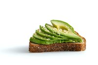 Fresh sliced avocado arranged in a fan pattern on whole grain toast, garnished with sesame seeds and black pepper on white background.