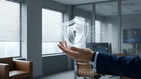 Businessman hand presenting holographic security shield icon in modern office environment for cybersecurity and data protection concepts.