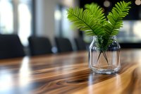 Fresh green palm leaves in glass vase on wooden conference table with blurred office background, minimalist modern workspace decor with natural elements.