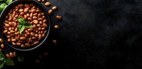 Raw peanuts in black ceramic bowl with fresh basil leaves on dark stone background with copy space for text, top view food photography.