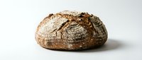 Freshly baked artisan sourdough loaf with crispy golden crust and scoring marks, isolated on white background for bakery, food, and culinary design projects.