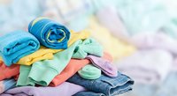 Colorful folded clothes pile with rolled towels and casual garments in bright hues for laundry, organization and household cleaning concepts.