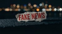 Crumpled newspaper with fake news headline on dark asphalt street with blurred city lights bokeh background at night for media literacy concepts.