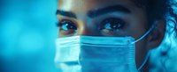 Young female medical worker wearing protective face mask in dramatic blue lighting, close up view of intense eyes and determined expression.