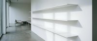 Modern minimalist interior with white floating shelves on wall, concrete floors, large windows creating clean architectural space for contemporary home or office design.