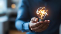 Glowing light bulb with geometric network pattern floating above businessman's palm against dark background, symbolizing innovation and creative solutions.