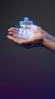 Hands holding glowing holographic puzzle piece with human figures representing teamwork and collaboration in business technology concept.