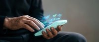 Businessman using smartphone with glowing digital icons and social media symbols floating above screen for modern communication and technology concepts.
