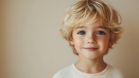 Portrait of young Caucasian child with blonde curly hair and blue eyes smiling against neutral beige background, conveying innocence and joy.