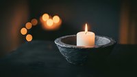 White candle burning in stone bowl with warm bokeh lights creating peaceful meditation atmosphere for spa relaxation and mindfulness practices.