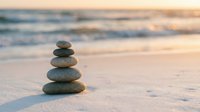 Zen stone stack balanced on sandy beach at golden sunset with soft ocean waves creating peaceful meditation and mindfulness atmosphere for wellness concepts.
