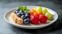 Fresh seasonal berries and fruits with granola bar served on white plate against gray background, healthy breakfast concept for food photography.