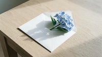 Blue hydrangea flower on white envelope placed on wooden table surface for greeting cards and romantic correspondence.